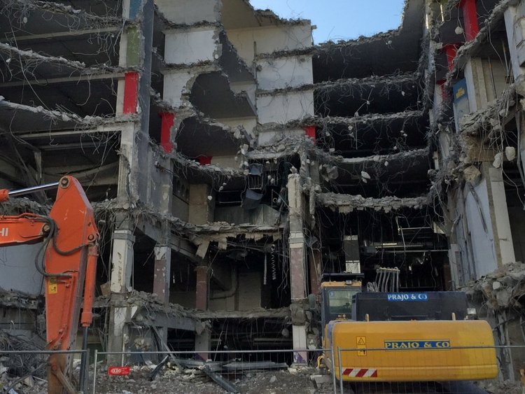 Foto: Abbruch Interspar Floridsdorf Wien: Blick auf ein teilweise abgerissenes Gebäude mit mehreren Geschossen; im Vordergrund der Arm eines Baggers und Baumaschinen