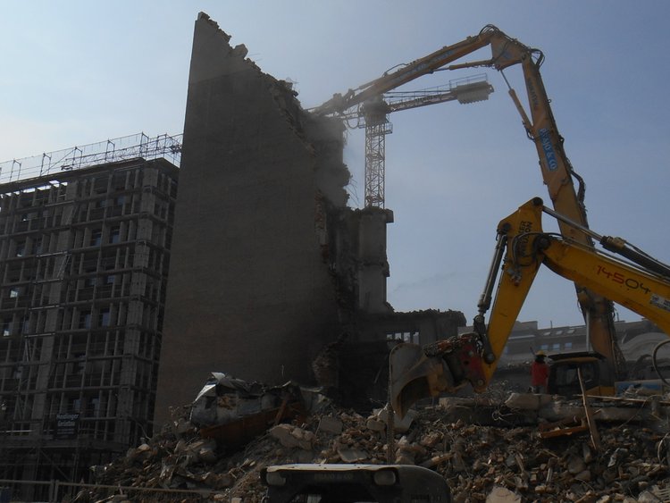 Foto: Post am Rochus: zwei Abbruchbagger über dem Schuttberg eines abgetragenen Gebäudes; daneben, von einer Feuermauer getrennt, ein eingerüsteter Rohbau